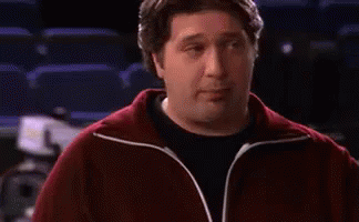 A Man In A Red Jacket Is Standing In Front Of A Sign That Says We . GIF