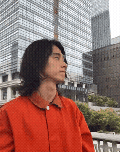 A Man In A Red Jacket Is Standing In Front Of A Tall Building GIF