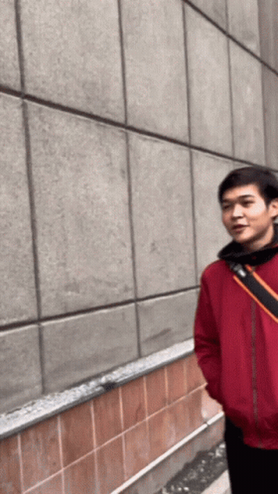A Man In A Red Jacket Is Standing In Front Of A Tiled Wall GIF
