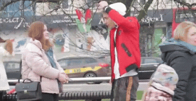 A Man In A Red Jacket Is Standing Next To A Woman In A Pink Jacket On A City Street . GIF