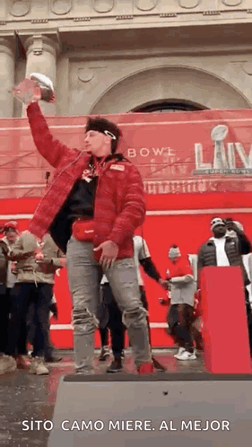 A Man In A Red Jacket Is Standing On A Stage Holding A Trophy In His Hand . GIF