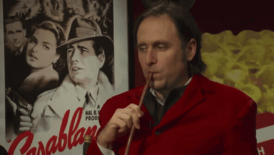 A Man In A Red Jacket Playing A Violin In Front Of A Poster For Parablan GIF