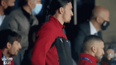 A Man In A Red Jacket Stands In A Crowd With The Word Futbol Karim On The Bottom Left GIF