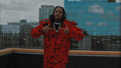 A Man In A Red Jacket Stands In Front Of A Building GIF