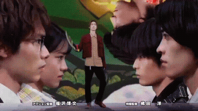 A Man In A Red Jacket Stands In Front Of A Group Of People With Asian Writing On The Bottom GIF