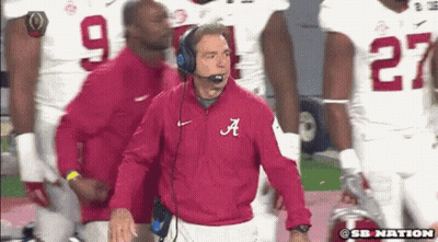 A Man In A Red Jacket With The Letter A On It Stands In Front Of A Group Of Football Players GIF