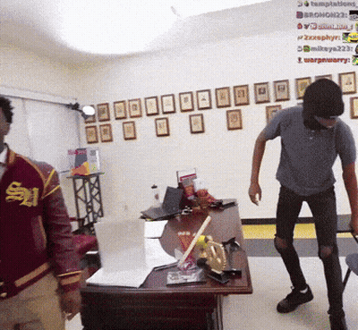 A Man In A Red Jacket With The Letter S On It Stands Next To Another Man GIF