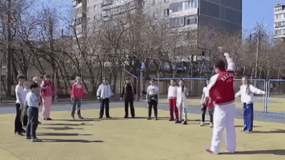 A Man In A Red Jacket With The Word Russia On It Is Standing In Front Of A Group Of Children On A Field . GIF