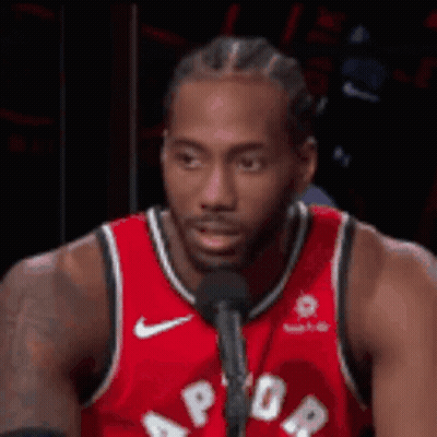 A Man In A Red Jersey Is Talking Into A Microphone . GIF