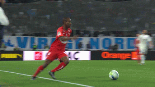 A Man In A Red Jersey Kicks A Soccer Ball On A Soccer Field GIF