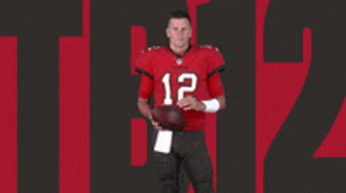 A Man In A Red Jersey With The Number 12 On It Holds A Football GIF