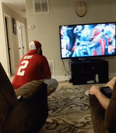 A Man In A Red Jersey With The Number 2 On It Sits In Front Of A Tv GIF