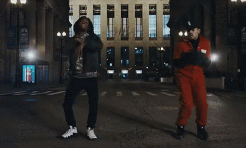 A Man In A Red Jumpsuit Is Dancing With Another Man GIF