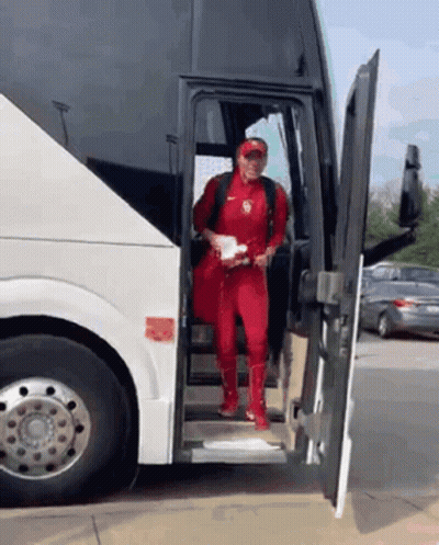 A Man In A Red Jumpsuit Is Getting Off A Bus GIF