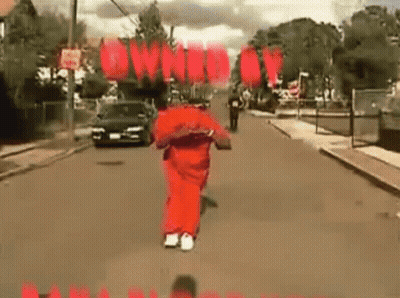 A Man In A Red Jumpsuit Is Running Down A Street With A Car Behind Him . GIF