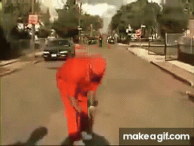 A Man In A Red Jumpsuit Is Standing On A Street . GIF