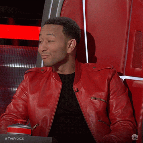 A Man In A Red Leather Jacket Is Sitting In A Chair With His Hand On His Chest .. GIF