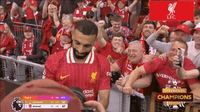 A Man In A Red Liverpool Jersey Stands In Front Of A Crowd GIF