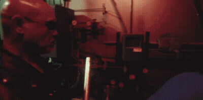 A Man In A Red Mask Is Standing In A Dark Room With A Red Light Behind Him GIF