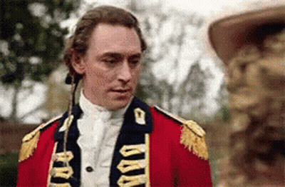 A Man In A Red Military Uniform Is Standing Next To A Statue . GIF