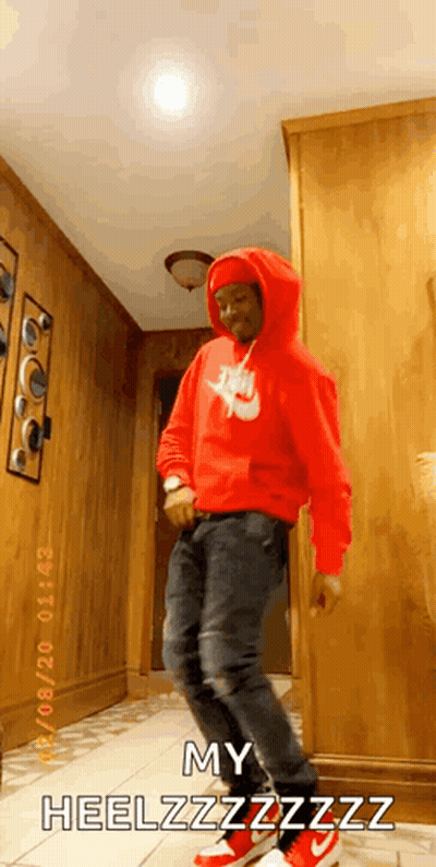 A Man In A Red Nike Hoodie Is Dancing In A Hallway While Wearing Red Sneakers . GIF