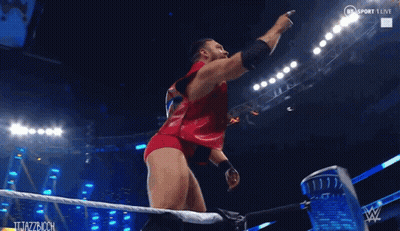 A Man In A Red Outfit Is Standing In A Wrestling Ring And Pointing At Something GIF