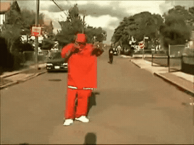 A Man In A Red Outfit Is Standing On The Street GIF