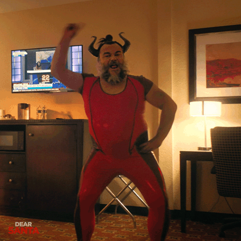 A Man In A Red Outfit With Horns Is Dancing In Front Of A Tv That Says Dear Santa GIF