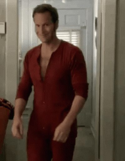 A Man In A Red Pajamas Is Walking Down A Hallway . GIF