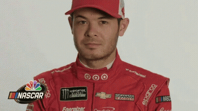 A Man In A Red Racing Suit And Hat Is Standing In Front Of A Nascar Sign . GIF