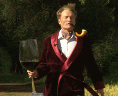 A Man In A Red Robe Holds A Glass Of Wine GIF