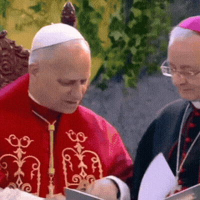 A Man In A Red Robe Is Sitting Next To Another Man In A Purple Hat GIF
