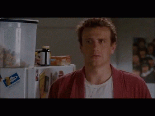 A Man In A Red Robe Is Standing In Front Of A Fridge With A Bottle Of Pills On It . GIF