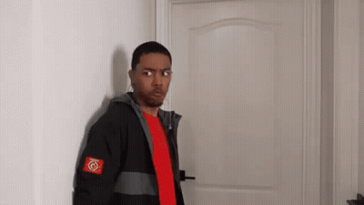 A Man In A Red Shirt And A Black Jacket Is Standing In Front Of A Door . GIF