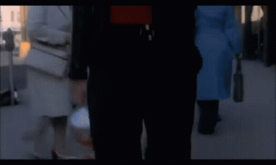A Man In A Red Shirt And A Black Jacket Is Walking Down The Street GIF