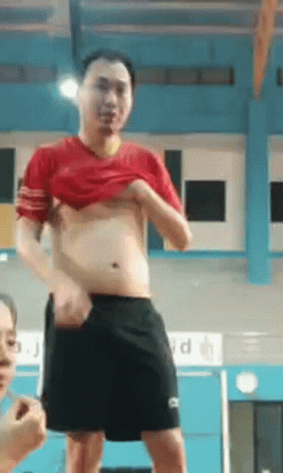 A Man In A Red Shirt And Black Shorts Has His Shirt Off GIF