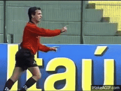 A Man In A Red Shirt And Black Shorts Stands In Front Of A Sign That Says " Itau " GIF