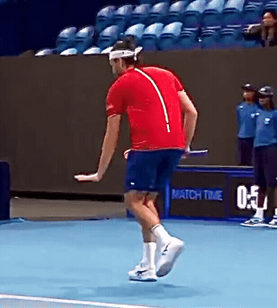 A Man In A Red Shirt And Blue Shorts Is Jumping On A Tennis Court . GIF