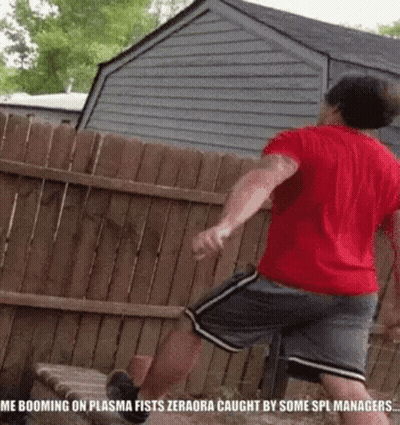A Man In A Red Shirt And Gray Shorts Is Jumping Over A Wooden Fence In Front Of A House . GIF