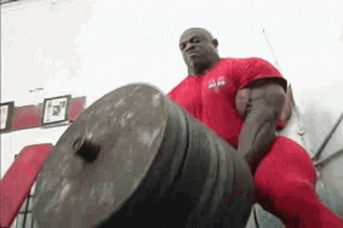 A Man In A Red Shirt And Red Pants Is Lifting A Large Weight . GIF