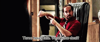A Man In A Red Shirt And Tie Is Sitting In A Chair And Says Three Hours Late What 'S The Deal GIF