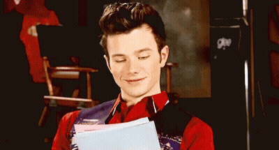 A Man In A Red Shirt And Vest Is Holding A Piece Of Paper And Smiling . GIF