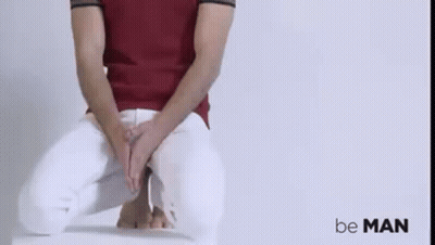 A Man In A Red Shirt And White Pants Is Sitting On A Chair With His Hands On His Lap . GIF