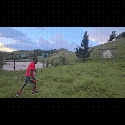 A Man In A Red Shirt Holds A Bow And Arrow In A Field GIF