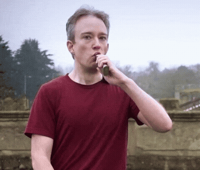 A Man In A Red Shirt Is Brushing His Teeth Outdoors GIF