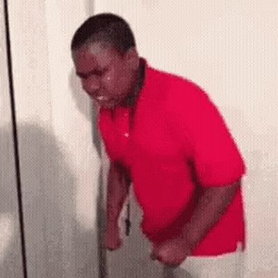 A Man In A Red Shirt Is Crying While Standing Next To A Door . GIF