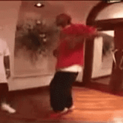 A Man In A Red Shirt Is Dancing On A Wooden Floor . GIF