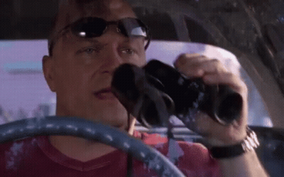 A Man In A Red Shirt Is Driving A Car And Looking Through Binoculars GIF