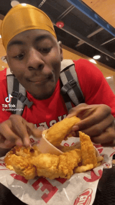 A Man In A Red Shirt Is Eating Fried Chicken And French Fries At A Fast Food Restaurant GIF