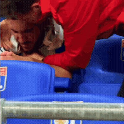 A Man In A Red Shirt Is Helping Another Man In A Stadium Seat GIF
